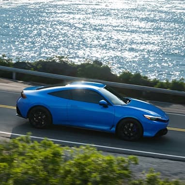 2027 Honda Prelude in Boost Blue Pearl driving through a costal road, profile view (exhilarating hybrid coupe).